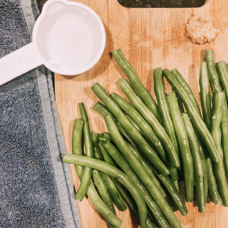 green beans on cutting board with blue towel and measuring cup